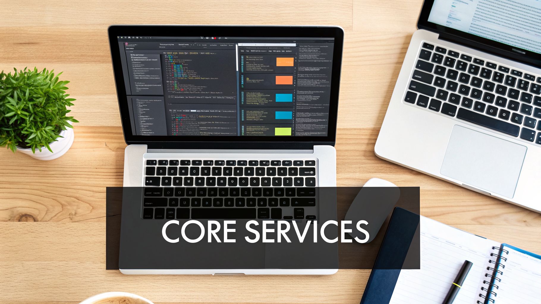 A top-down view of a developer's workspace with two laptops, code on screen, and desk items.