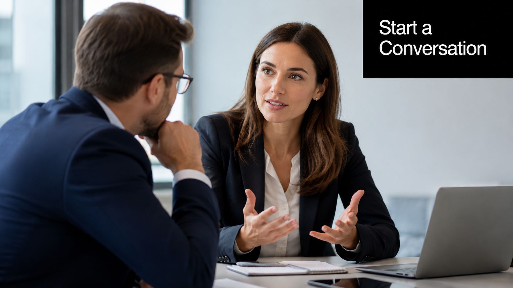 A professional man and woman having a productive business conversation while working at a desk with laptop