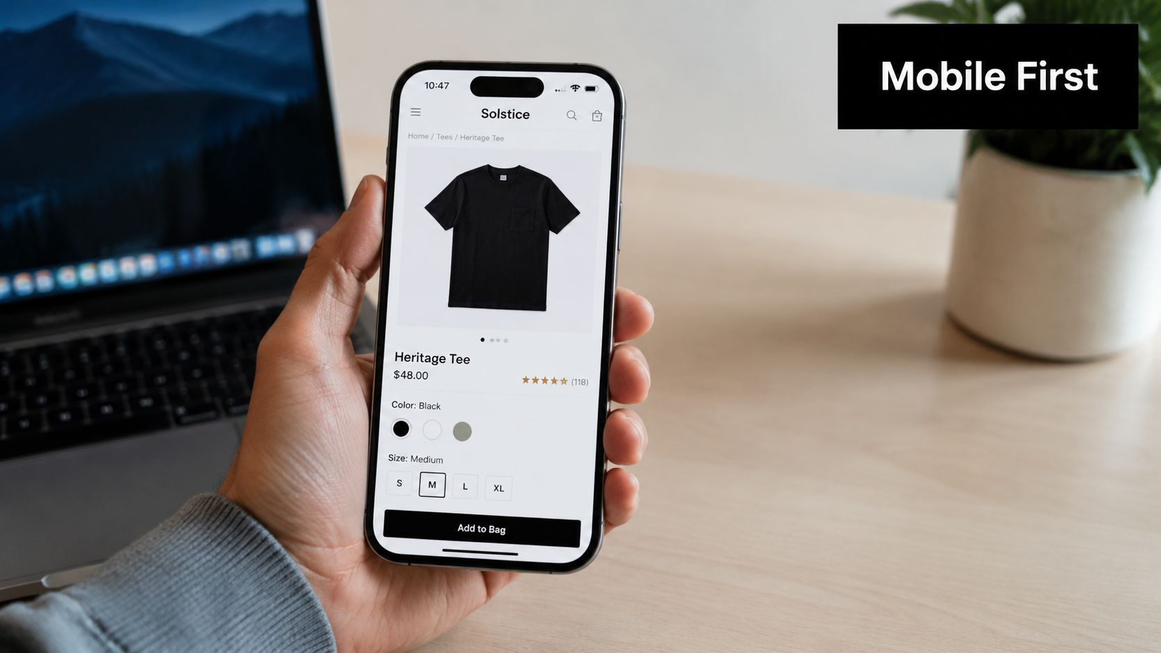 A hand holding a smartphone displaying a mobile ecommerce product page for a black t-shirt.